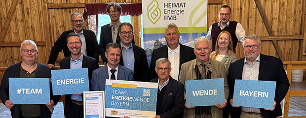 11 Männer und eine Frau stehen nebeneinander und lächeln in die Kamera während sie blaue Schilder hochhalten auf denen steht "Team Energiewende Bayern"
