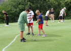 Mehrere Jugendliche stehen auf einem grünen Platz, halten Golfschläger in der Hand und konzentrieren sich mit Blick nach unten auf ihre Golfbälle.